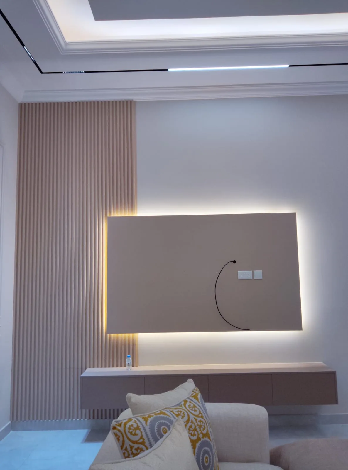 Backlit TV panel beside vertical fluted slats with a floating media shelf