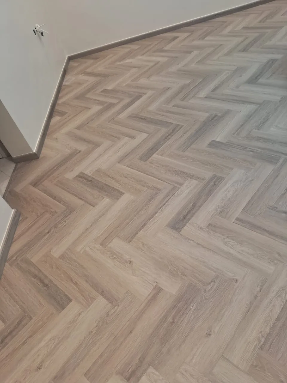 Herringbone oak-effect flooring laid through a hallway with matching skirting