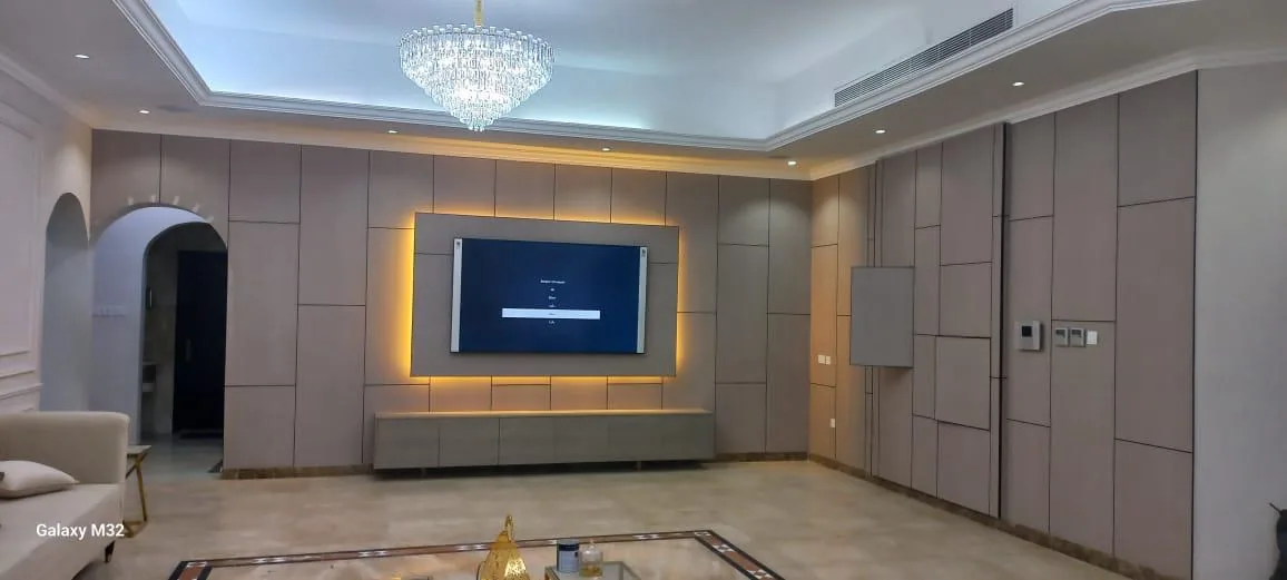 Wide majlis with full-height wall panelling, backlit TV wall and crystal chandelier