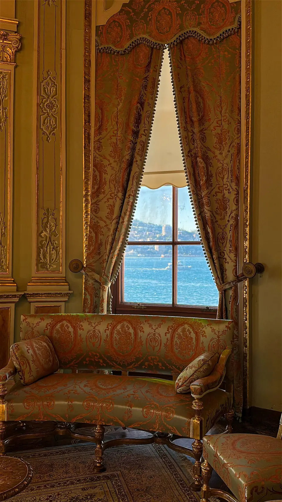 Ornate damask curtain drapery framing a window with a sea view