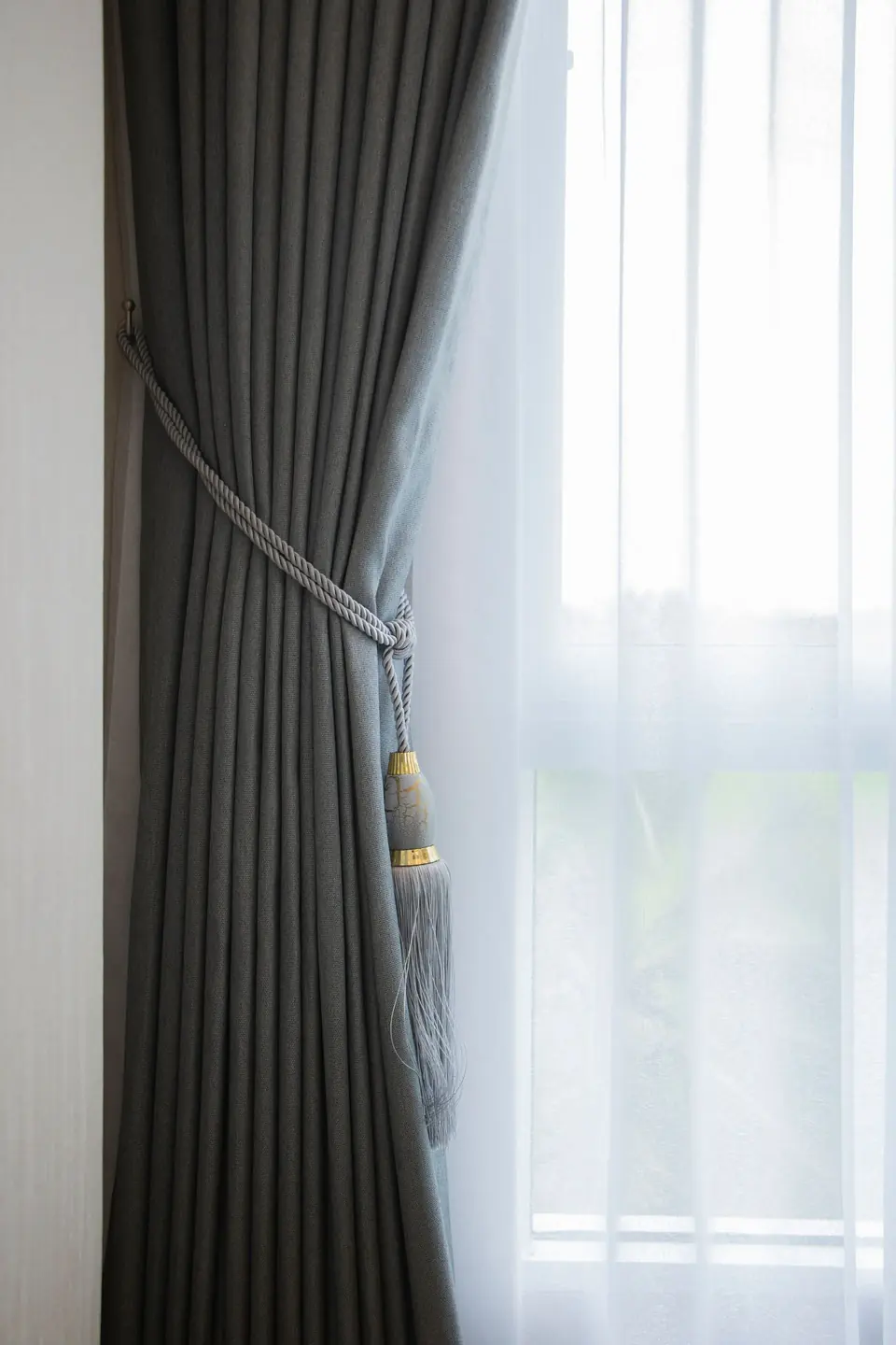 Close-up detail of soft grey curtain fabric with decorative tassel tieback
